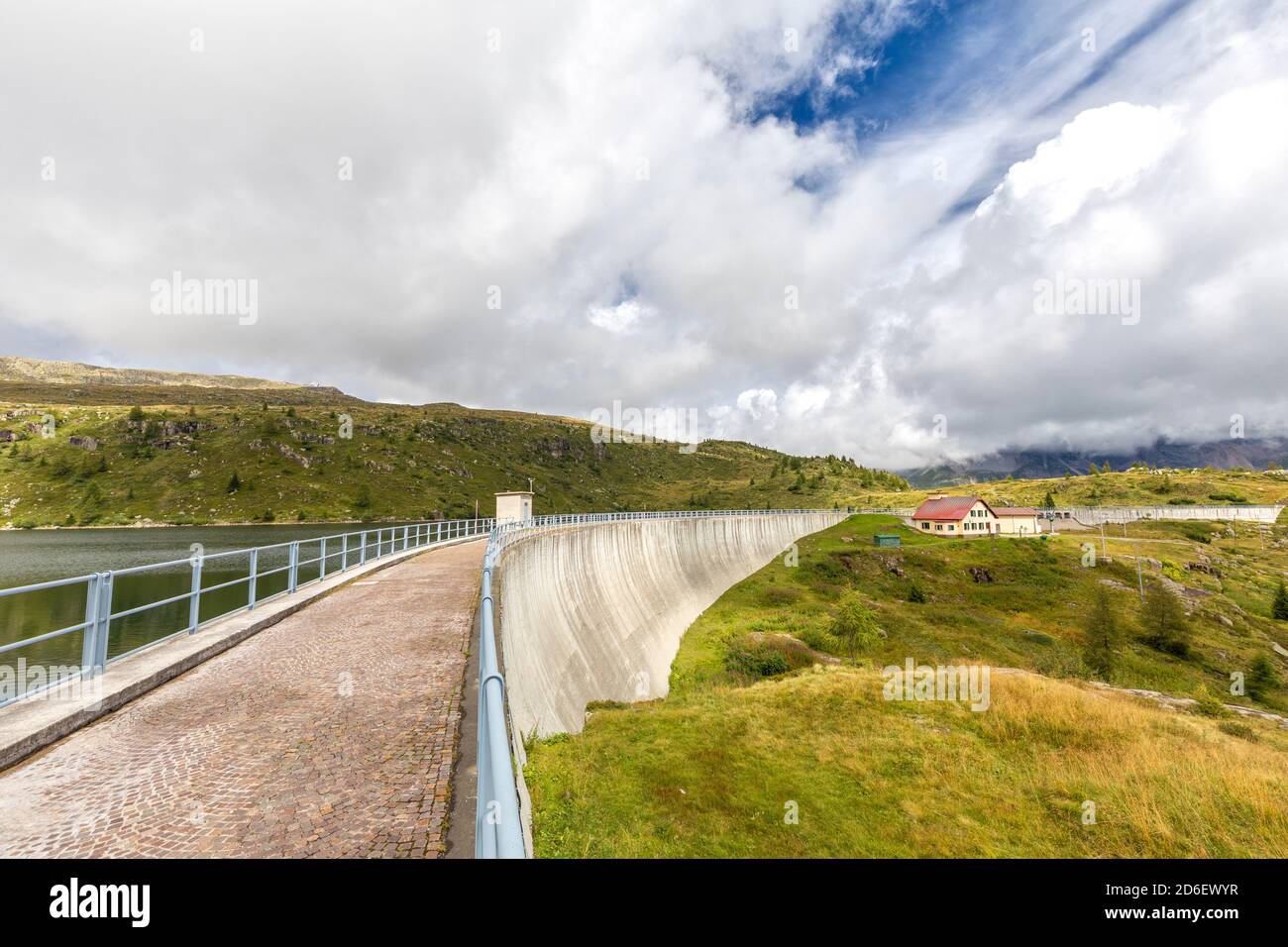 Der Weg des Cavia Staudamms mit Lago del Cavia an einem bewölkten Tag, das Schutzhaus mit dem roten Dach, falcade, belluno, venetien, Italien Stockfoto