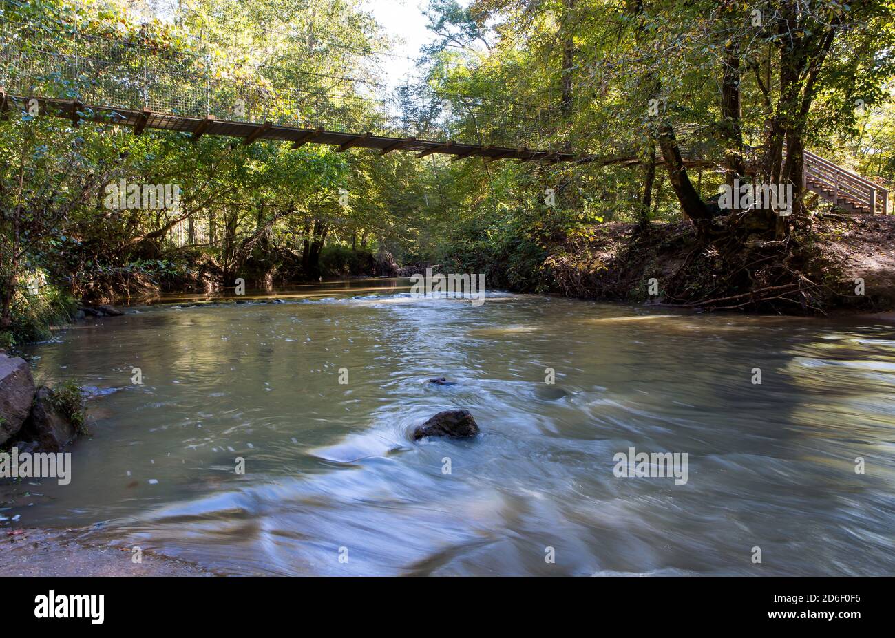 Eine schwingende Fußgängerbrücke überspannt einen rauschenden Bach in einem bewaldeten Schutzgebiet. Stockfoto