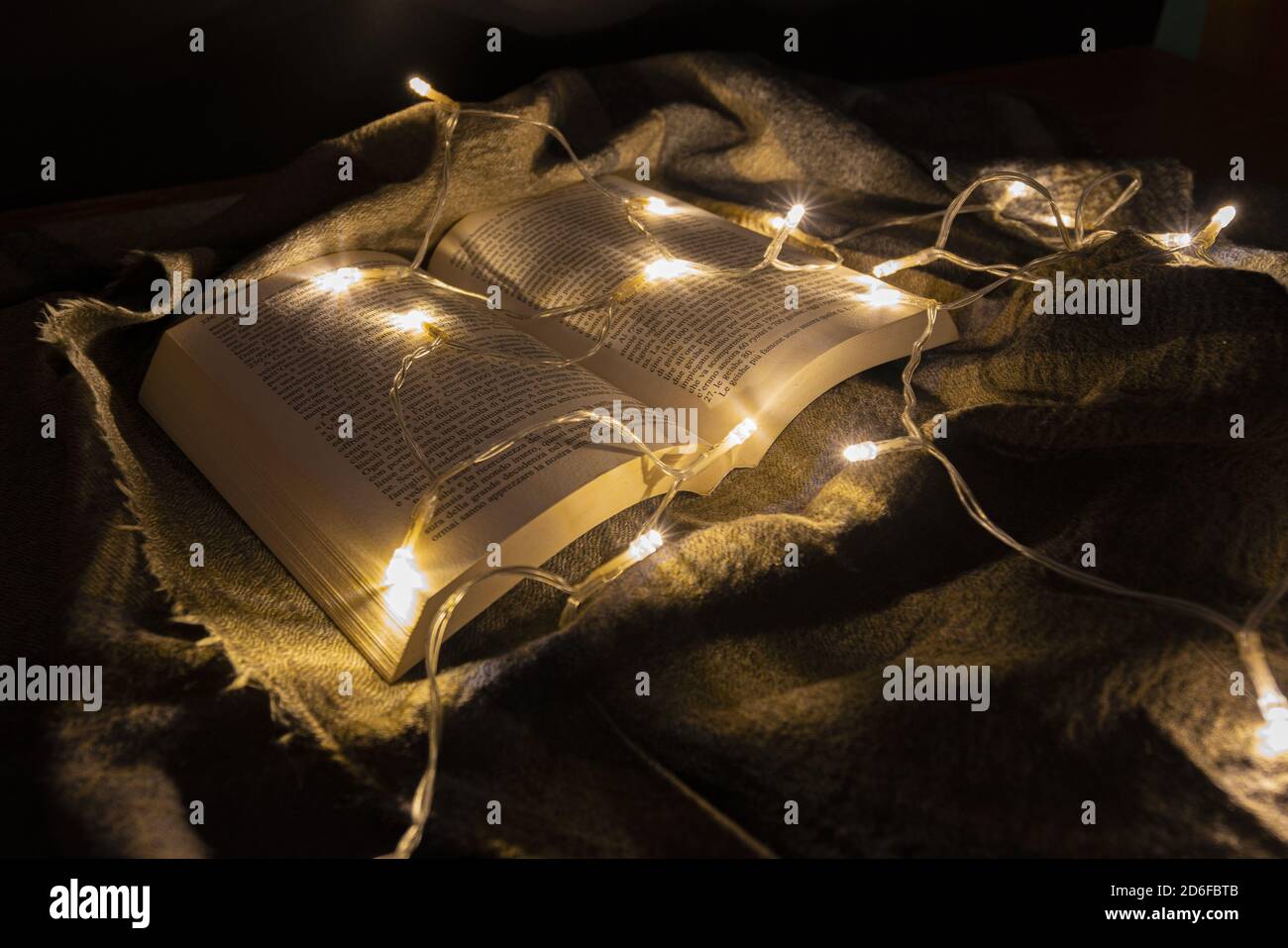 Kleine weiße Lichter beleuchten ein Buch, das auf einer Wolle platziert ist Decke Stockfoto