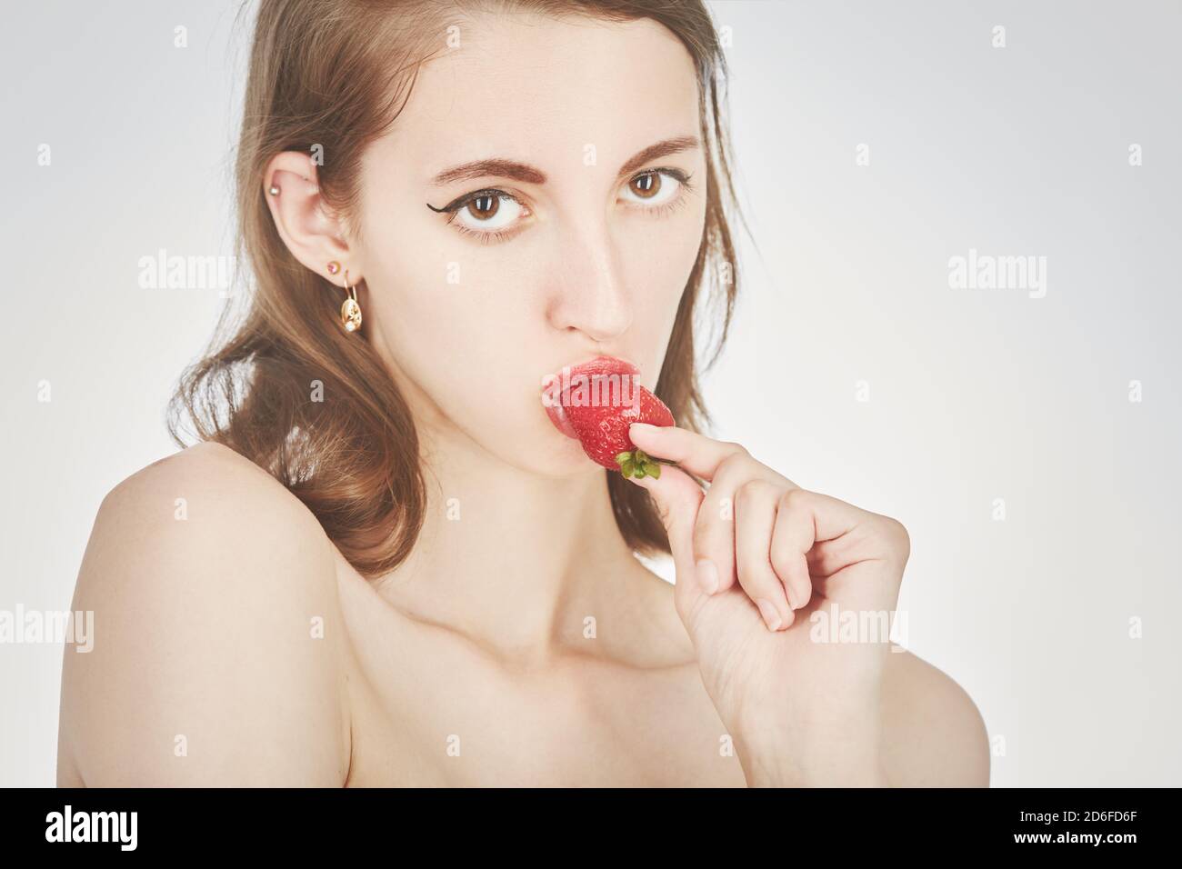 Junge Frau isst saftige Erdbeere auf weißem Hintergrund, Blick auf die Kamera Stockfoto