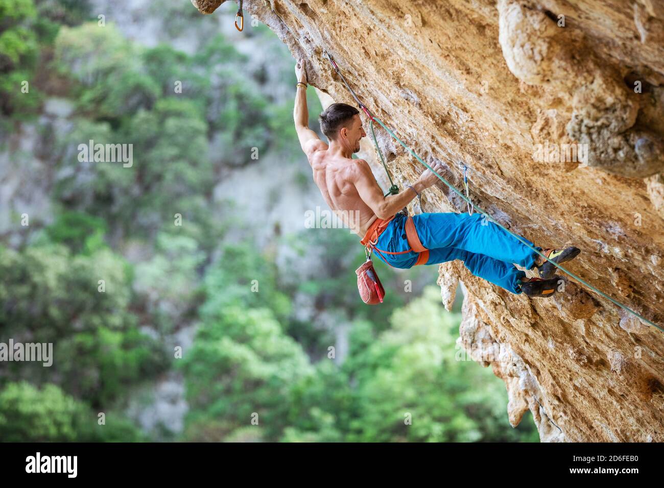 Felskletterer an überhängender Wand. Klettern auf natürlichen Klippen. Starker junger Mann, der sich bemüht, kleine Handgriffe auf anspruchsvoller Strecke zu greifen. Stockfoto