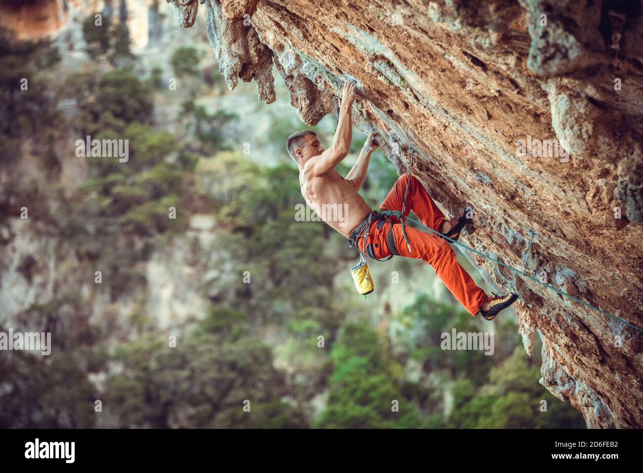 Junger männlicher Kletterer an überhängender Wand. Klettern auf natürlichen Klippen. Starker junger Mann kämpft sich anspruchsvolle Route. Stockfoto