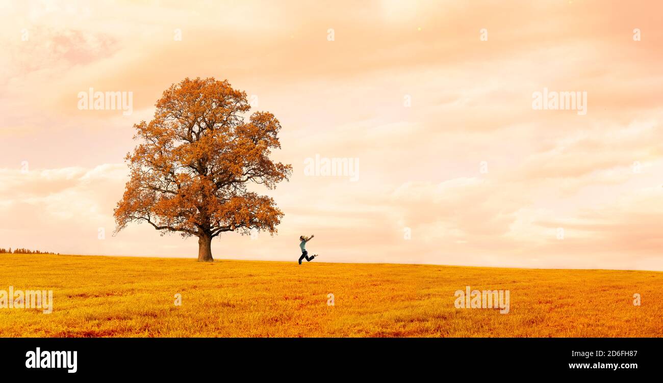 Frau läuft glücklich auf einer Wiese mit einem Baum in Herbst Stockfoto