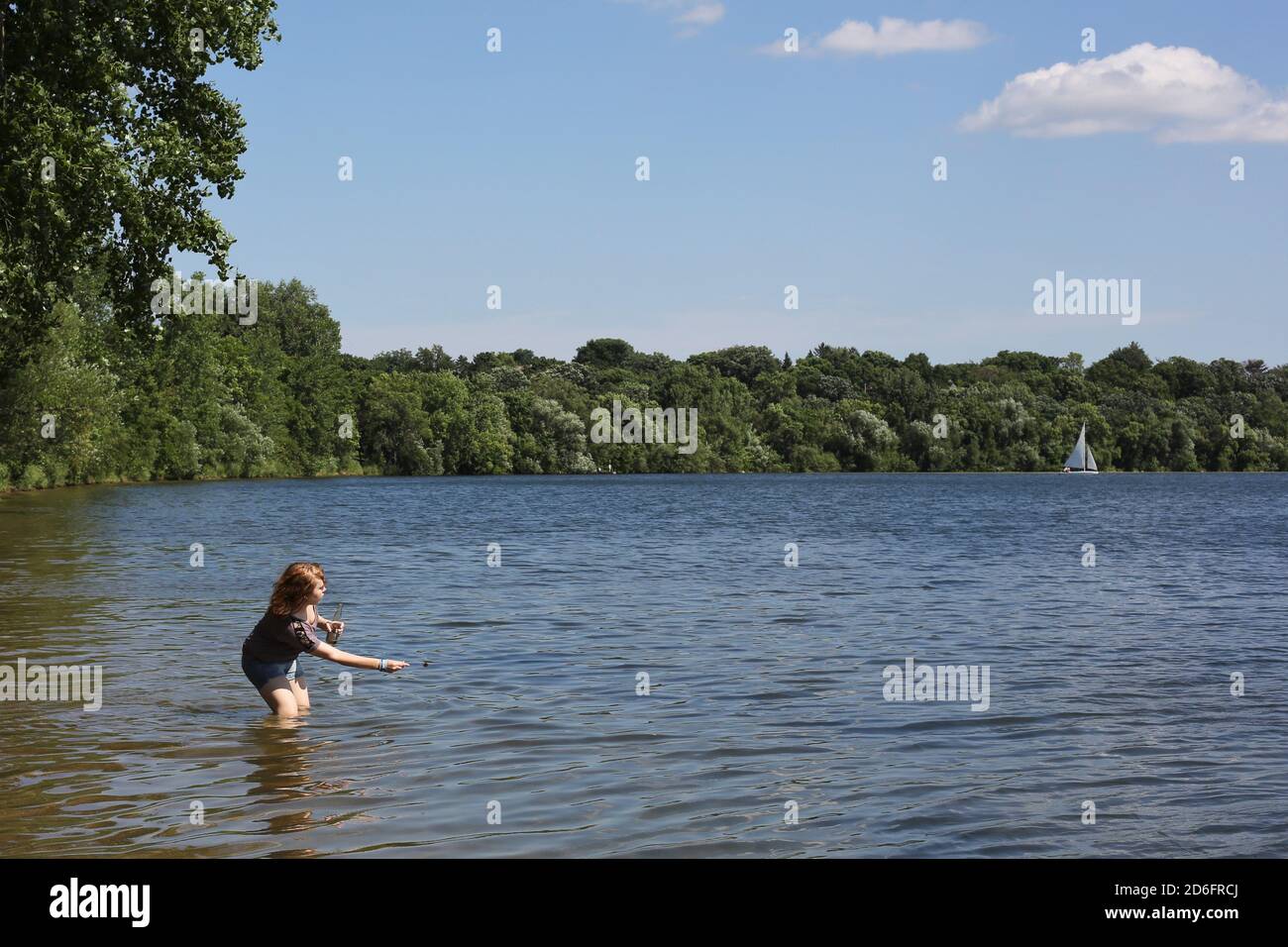 Ein jugendliches Mädchen, das in einem See steht und ein abgefülltes Getränk hält und einen Felsen überspringt. Stockfoto