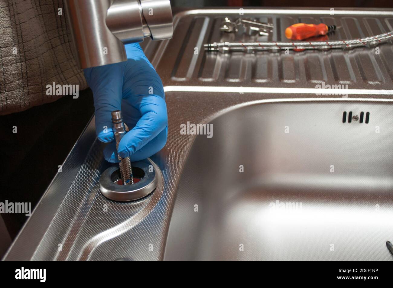 Installation des Wasserhahns an einem Waschbecken. Hände halten eine Küchenarmatur mit elastischen Schläuchen. Reparatur eines Wasserhahns. Stockfoto