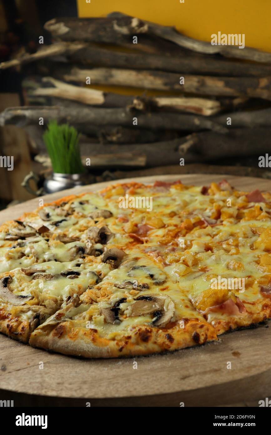Vertikale Aufnahme einer leckeren Pizza mit Pilzen, Ananas und Schinken auf einem Holzbrett auf dem Tisch Stockfoto