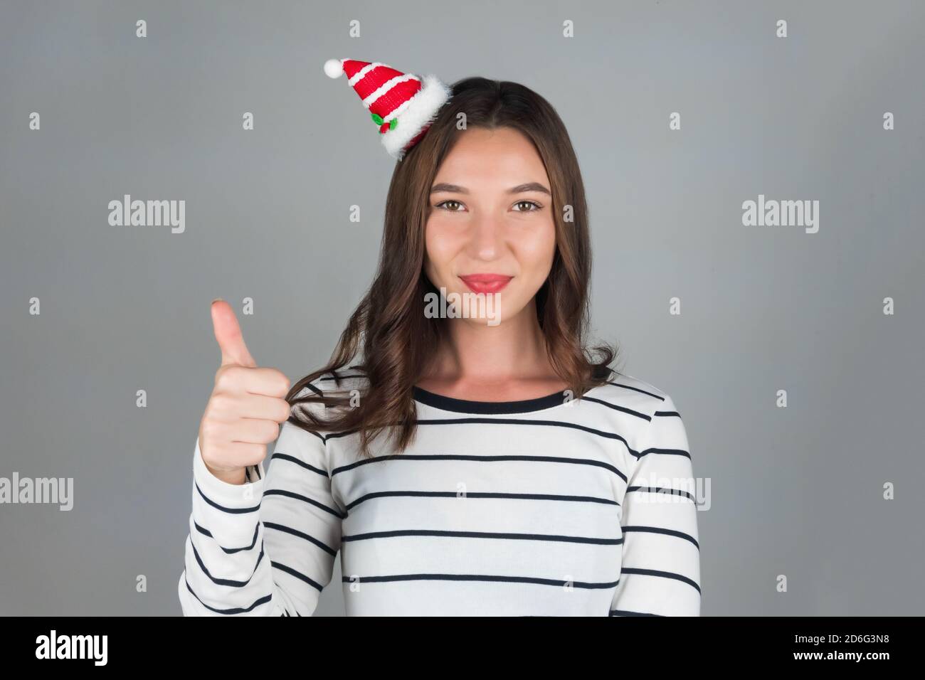 Ein junges Mädchen mit weihnachtlicher Dekoration im Haar posiert für ein Auto. Halten Sie Ihre Finger oben, positive Emotionen. Hochwertige Fotos Stockfoto