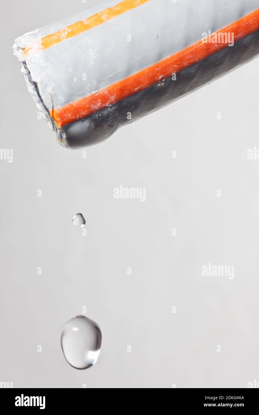 Extreme Nahaufnahme eines Wassertropfens, der aus einem tropft Schlauch - grauer Hintergrund Stockfoto