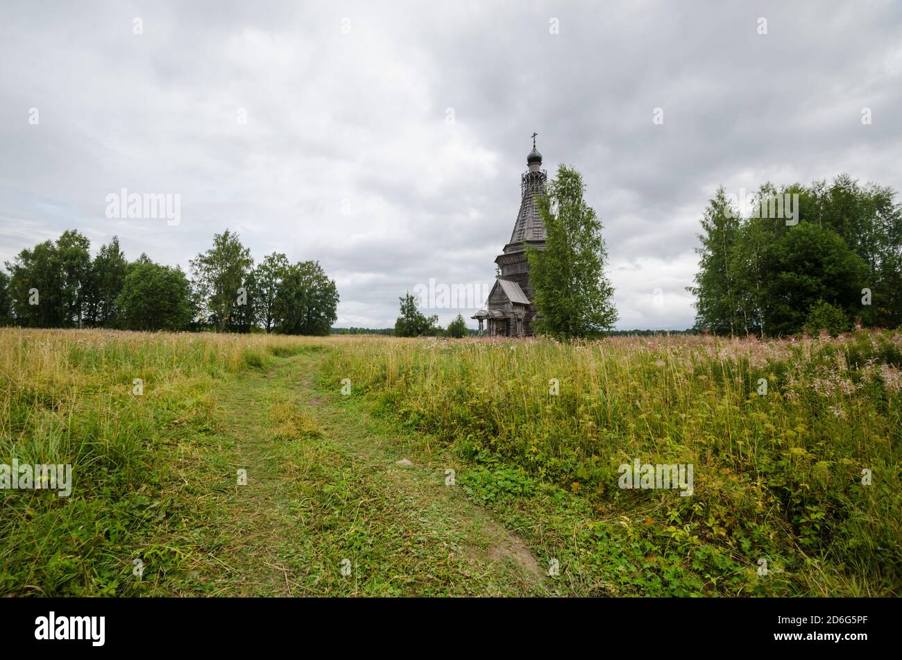 August 2020 - Red Lag. Verlassene hohe Holzkirche in der Mitte eines großen Feldes. Russland, Archangelsk Region Stockfoto