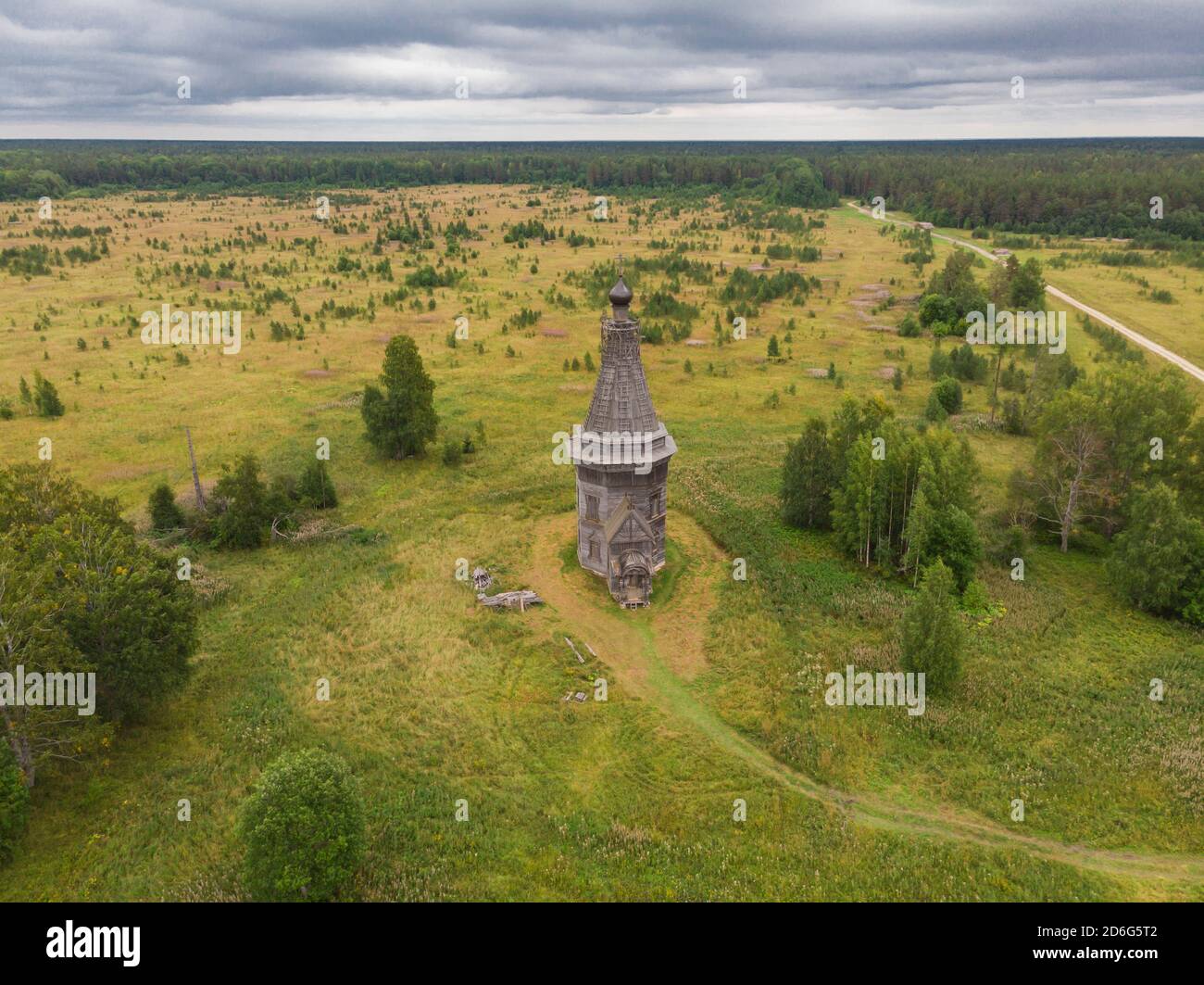 August 2020 - Red Lag. Verlassene hohe Holzkirche in der Mitte eines großen Feldes. Russland, Archangelsk Region Stockfoto