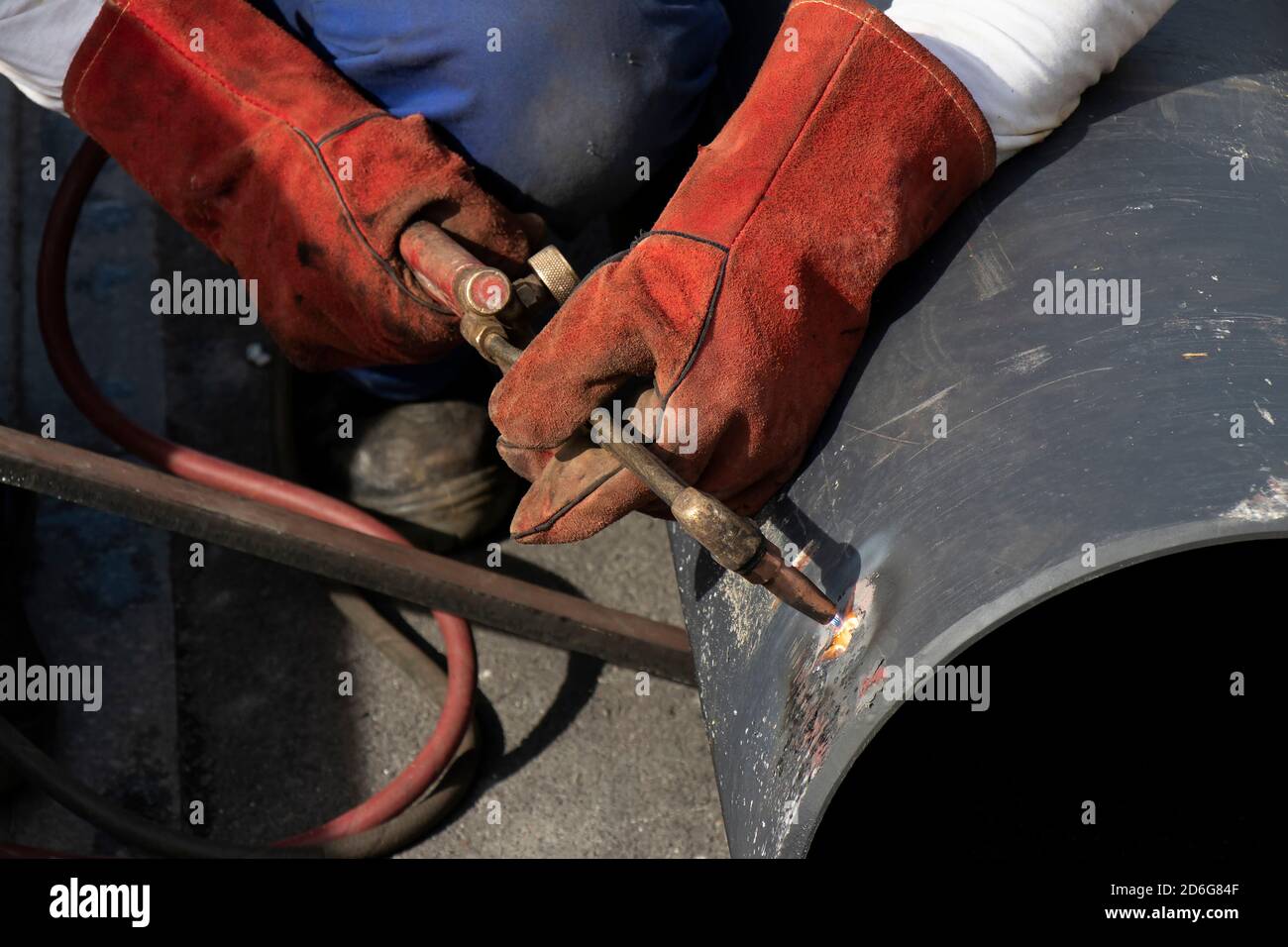 Schweißer Arbeiter schweißen ein breites Metallrohr mit einem Oxy-Fuel-Schneidbrenner., Nahaufnahme Detail der Hände und Brennergriff Stockfoto