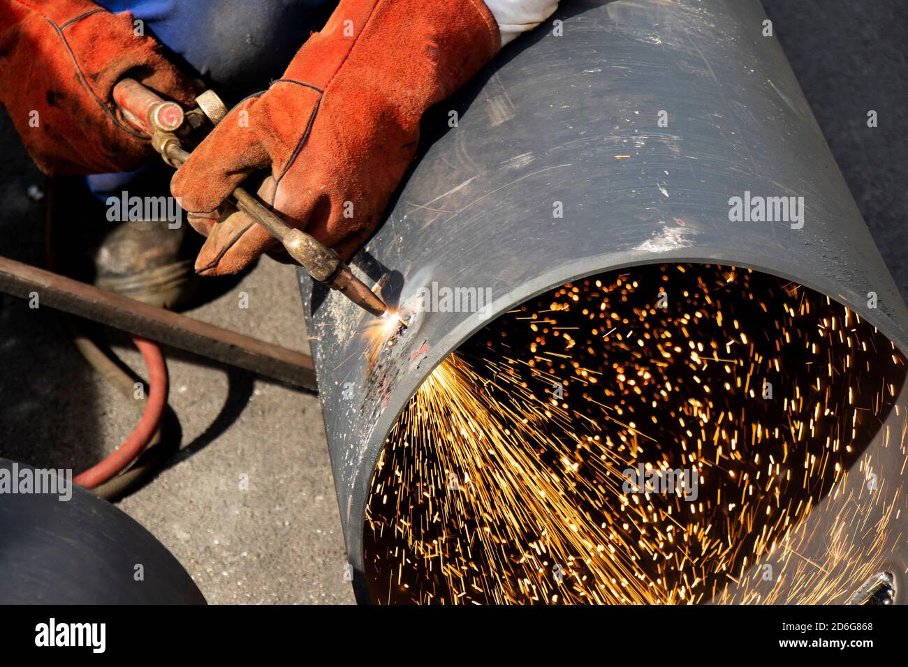 Schweißer Arbeiter Hände Schweißen ein breites Metallrohr mit einem Oxy-Fuel-Schneidbrenner, mit Flamme und Funken, Nahaufnahme Detail, auf der Baustelle Stockfoto