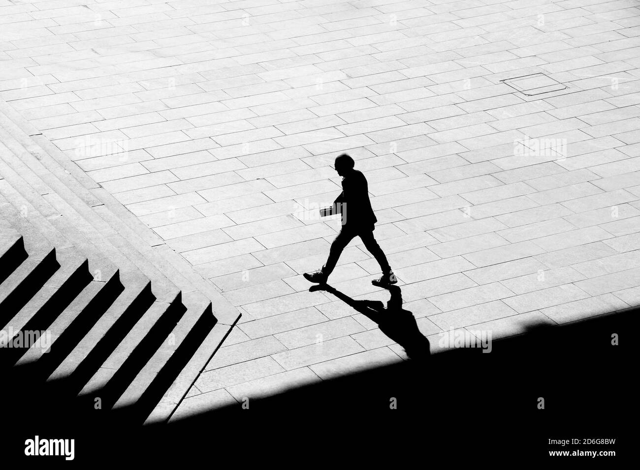 Belgrad, Serbien - 09. Oktober 2020: Schattensilhouette eines Mannes, der Papiere hält, während er auf dem Bürgersteig des Stadtplatzes zur Treppe eines öffentlichen Gebäudes geht, Stockfoto