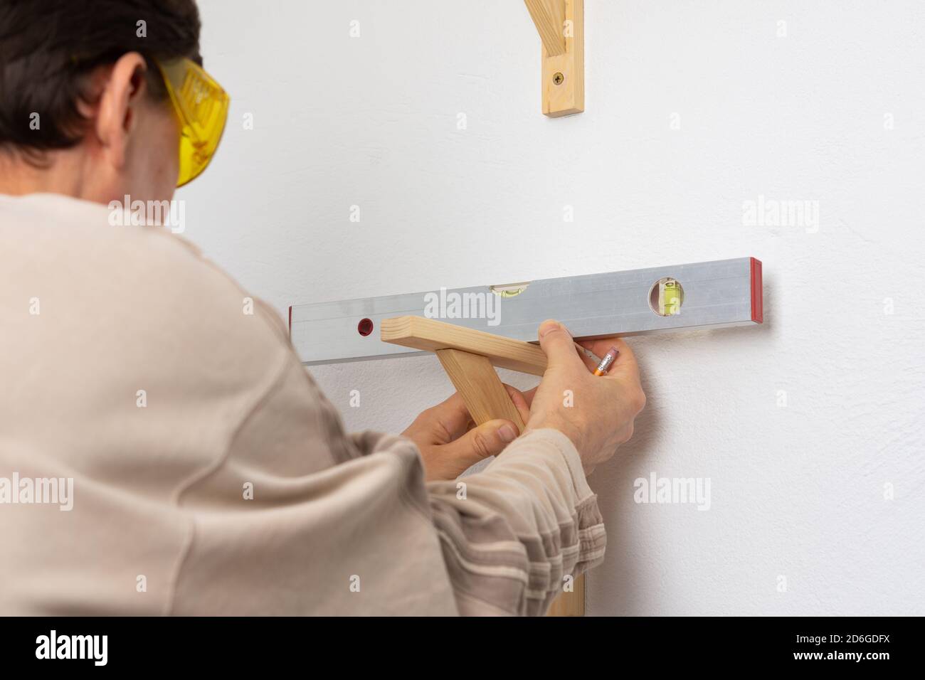 Ein Mann hängt ein Regal in einer Wohnung an einer weißen Wand, ein Arbeiter überprüft die Ebenheit des Regals mit einer Spint-Ebene Stockfoto