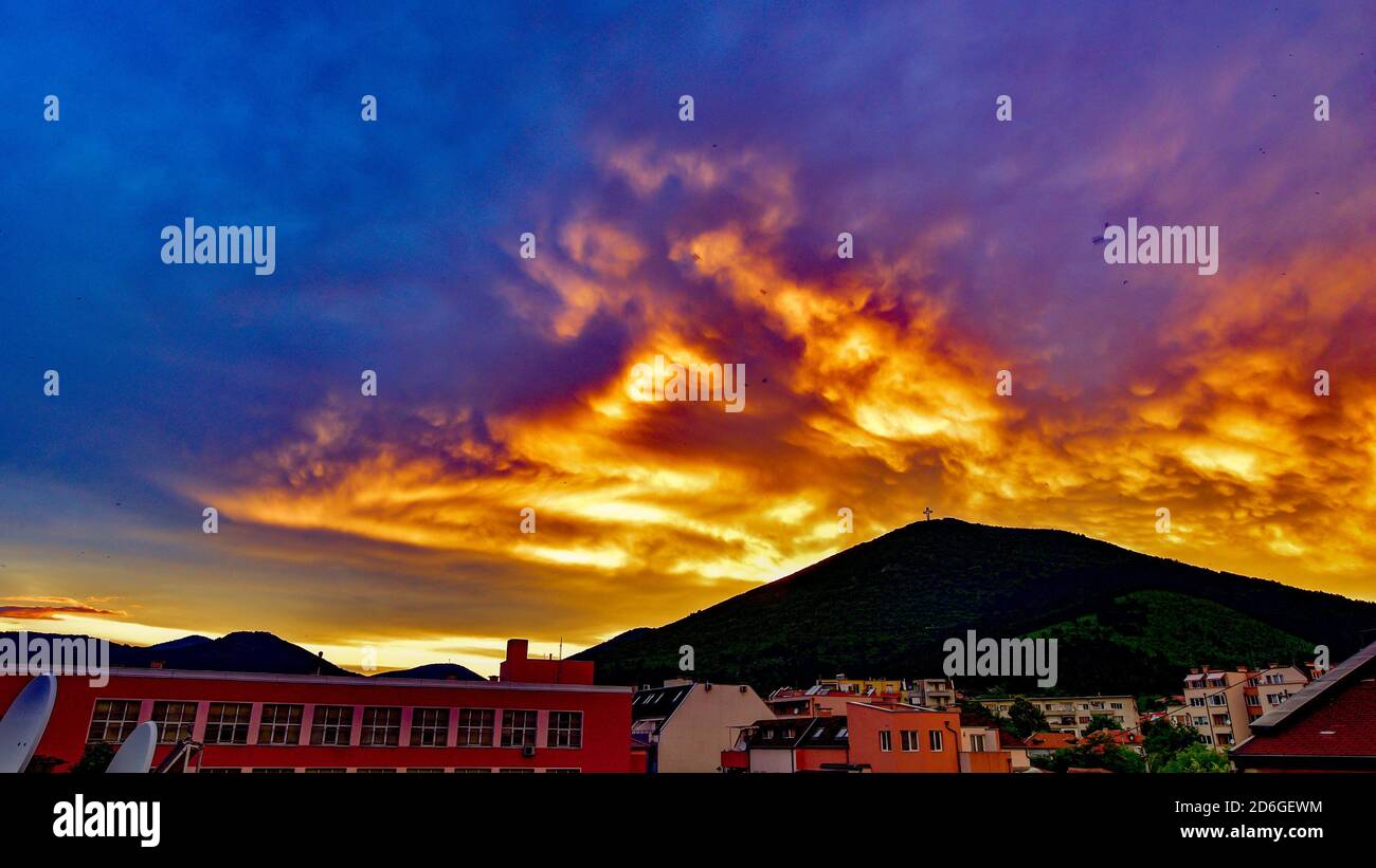 Brennender Sonnenuntergang Himmel und Wolkenlandschaft über einer Stadt in der Nähe von A Berg Stockfoto