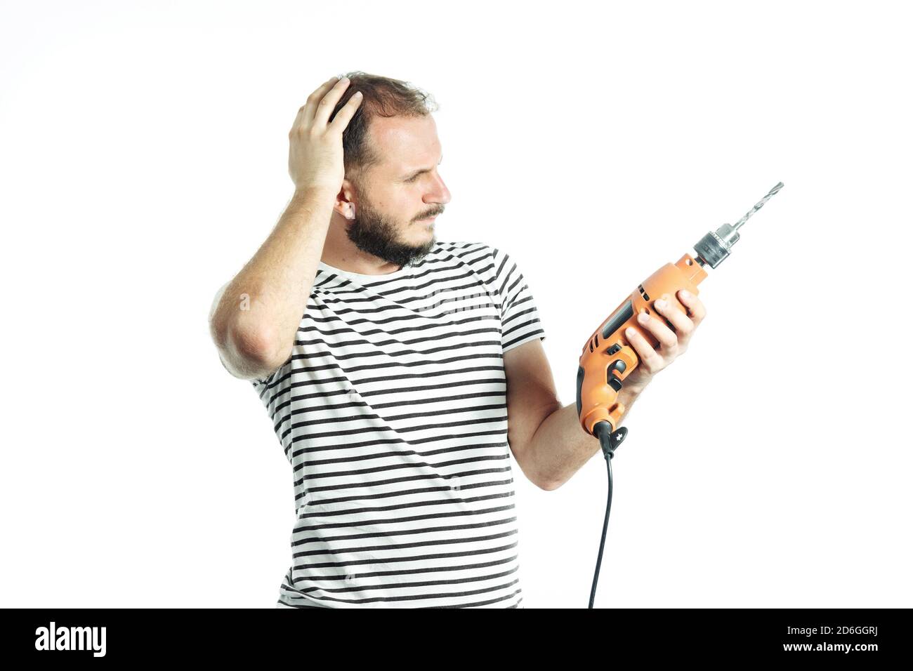 Ein Arbeiter in Ratlosigkeit überlegte Blick auf ein Elektrowerkzeug - elektrische Bohrmaschine. Isoliert auf Weiß Stockfoto