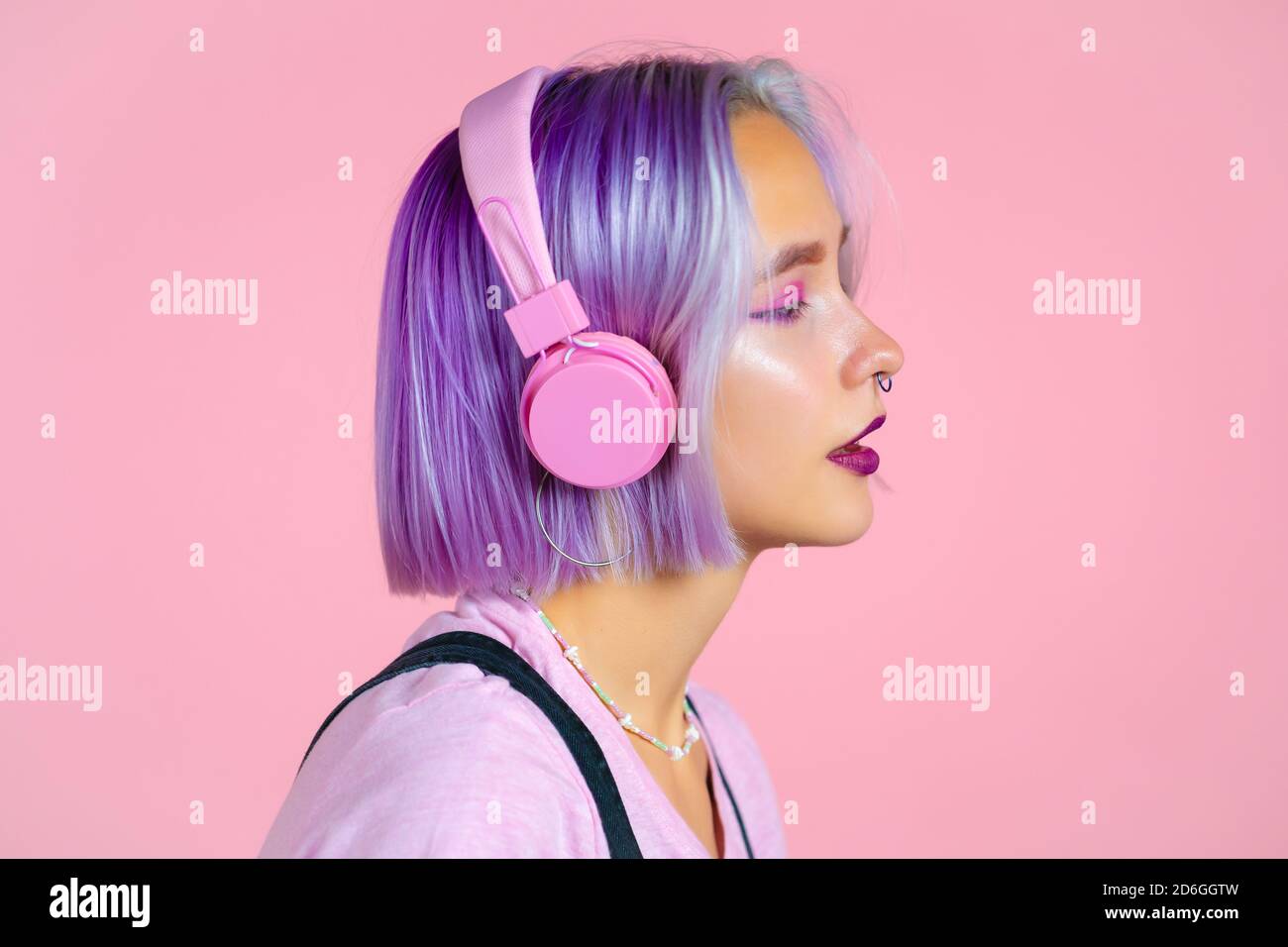 Nahaufnahme Porträt von hübschen Mädchen mit gefärbten violetten Haaren Musik hören, lächeln, tanzen in Kopfhörer im Studio vor rosa Hintergrund. Musik Stockfoto