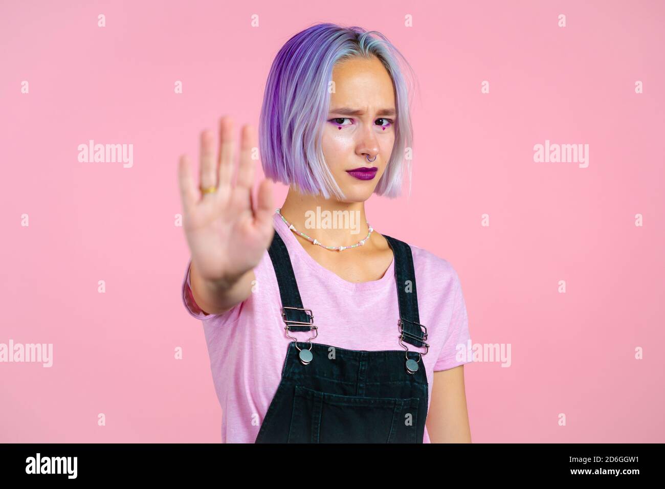 Hübsche Frau mit violettem Haar missbilligend ohne Handzeichen Geste. Leugnen, ablehnen, nicht zustimmen, Porträt von schönen Hipster Mädchen auf rosa Stockfoto