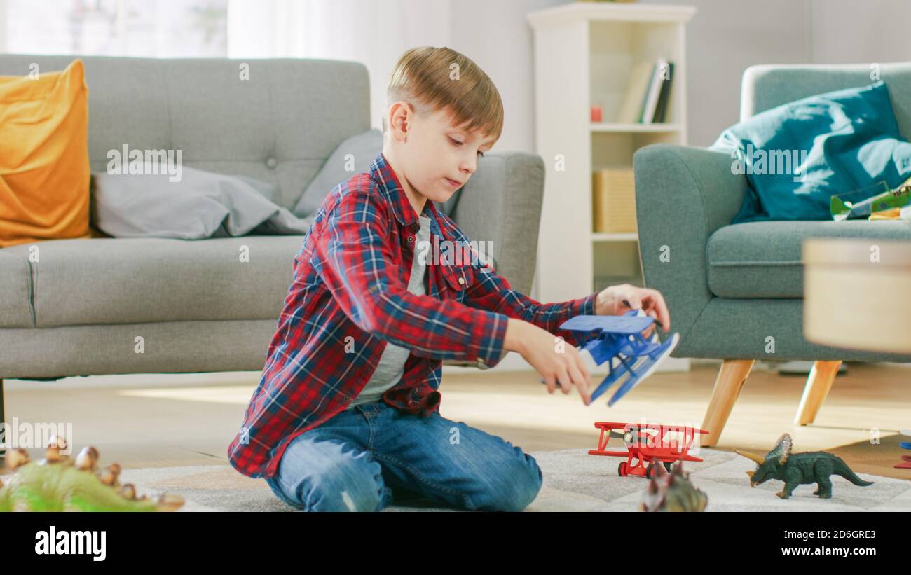 Zu Hause: Smart Little Boy spielt mit Spielzeug Flugzeug. Kleines Kind spielt auf einem Teppich im sonnigen Wohnzimmer. Stockfoto