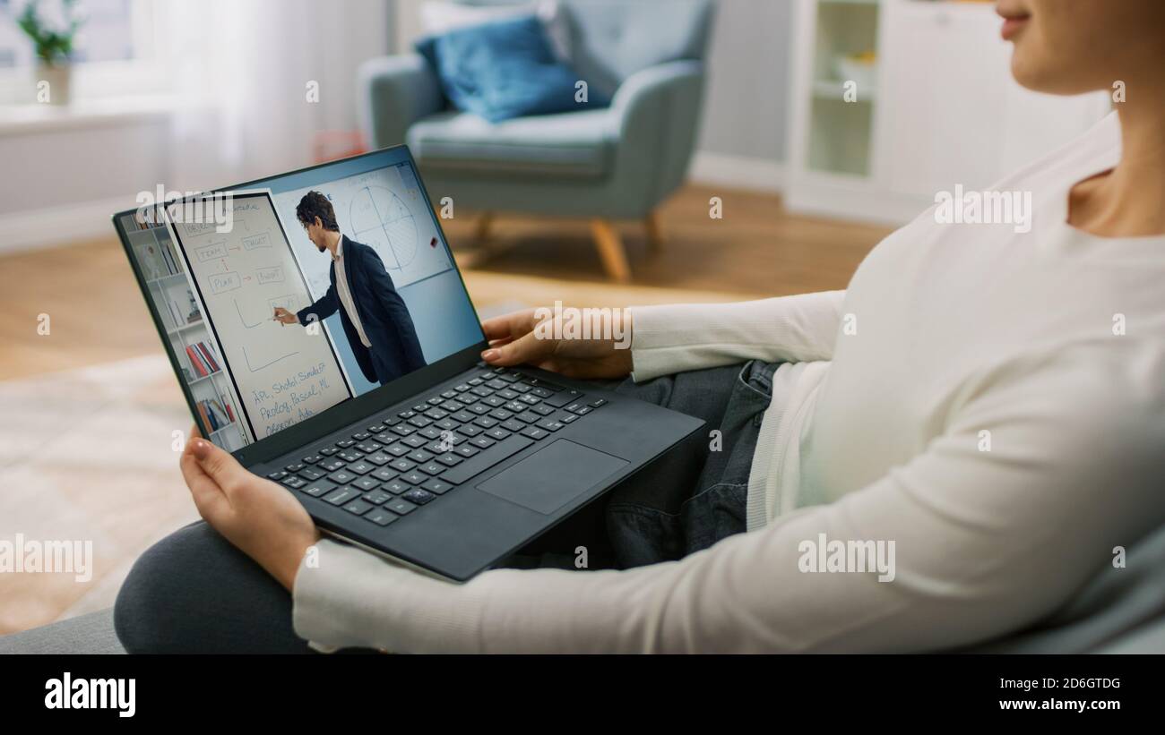 Junge Frau zu Hause verwendet Laptop für Video-Anruf mit seinem Lehrer. Bildschirm zeigt Online-Vortrag mit Lehrer erklärt Mathematik Thema. Er sitzt darauf Stockfoto