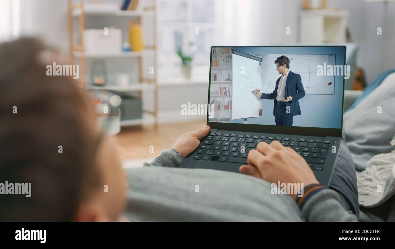 Mann zu Hause Laying auf einer Couch mit Laptop-Computer für Videoanruf an seinen Lehrer. Bildschirm zeigt Online-Vortrag mit Lehrer erklärt Mathematik Thema. Stockfoto
