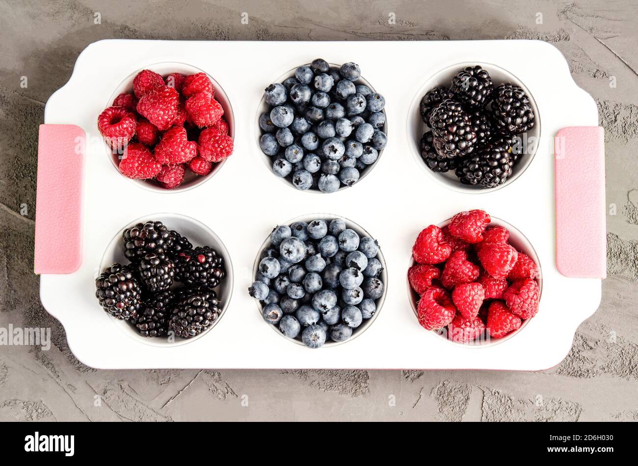 Frische Himbeeren, Blaubeeren und Brombeeren in einer weißen Eisenkalzform auf grauem Betongrund. Nahaufnahme, Saisonkonzept, Sommersaison. Er Stockfoto