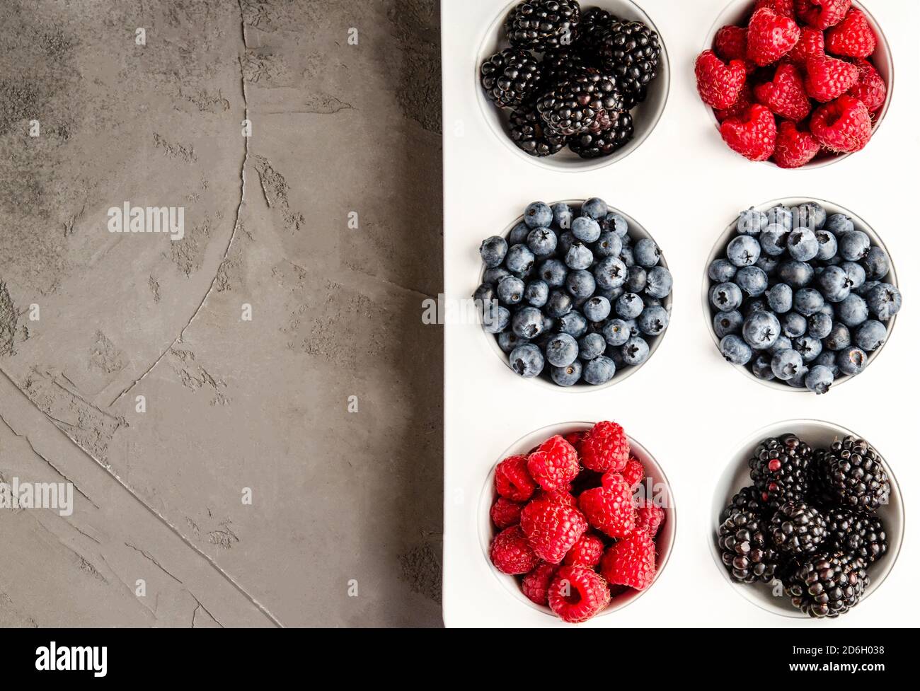 Frische Himbeeren, Blaubeeren und Brombeeren in einer weißen Eisenkalzform auf grauem Betongrund. Nahaufnahme, Platz kopieren, Saisonkonzept, Summe Stockfoto