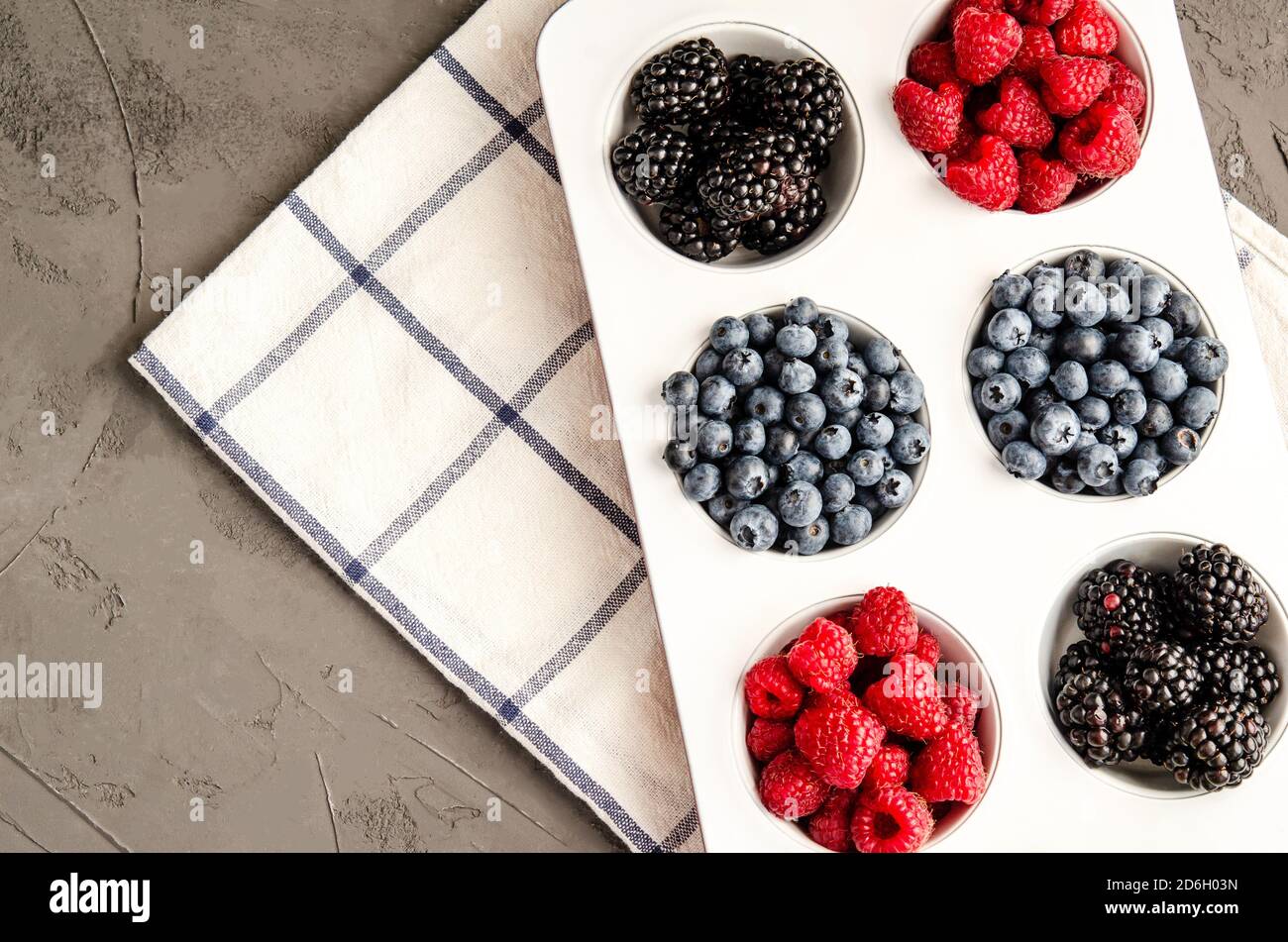 Frische Beeren Himbeeren, Heidelbeeren und Brombeeren im Weißeisenbacken, mit Serviette auf grauem Betongrund. Nahaufnahme, Platz kopieren, Saison Stockfoto
