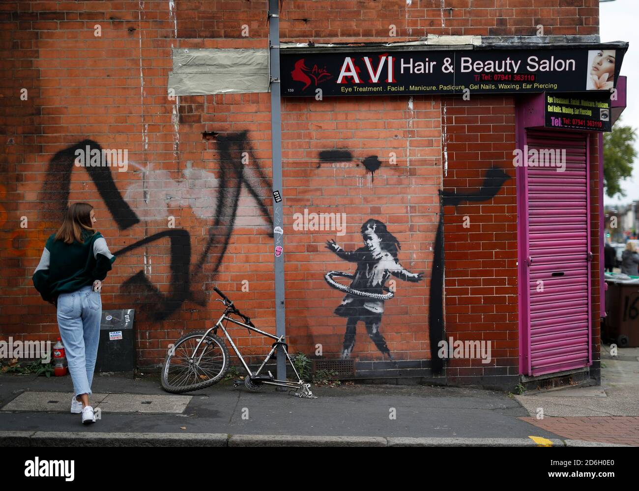 Nottingham, Nottinghamshire, Großbritannien. Oktober 2020. Eine Frau betrachtet ein Werk der Graffiti-Künstlerin Banksy. Die Arbeit, außerhalb eines Schönheitssalons, zeigt ein Mädchen Hula-Hooping mit einem Fahrradreifen neben einem Fahrrad, das sein Hinterrad fehlt. Credit Darren Staples/Alamy Live News. Stockfoto