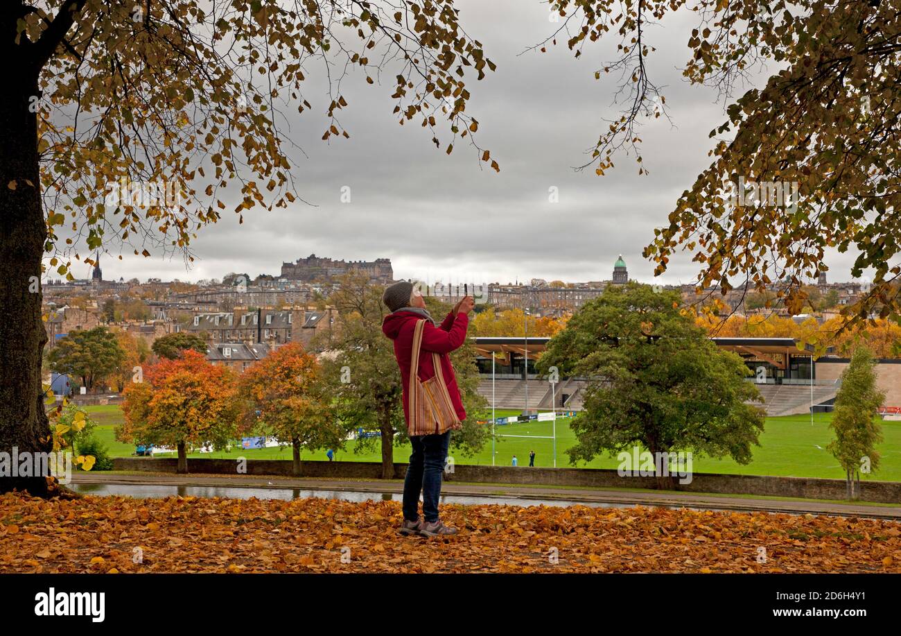 Inverleith Park, Edinburgh, Schottland, Großbritannien. 17. Oktober 2020. An einem bewölkten Tag verlieren die Bäume ihre Herbstfarben in Inverleith mit der Skyline der Innenstadt im Hintergrund. Eine Dame nimmt mit ihrem Handy einen Fotoaph. Quelle: Arch White/Alamy Live News Stockfoto