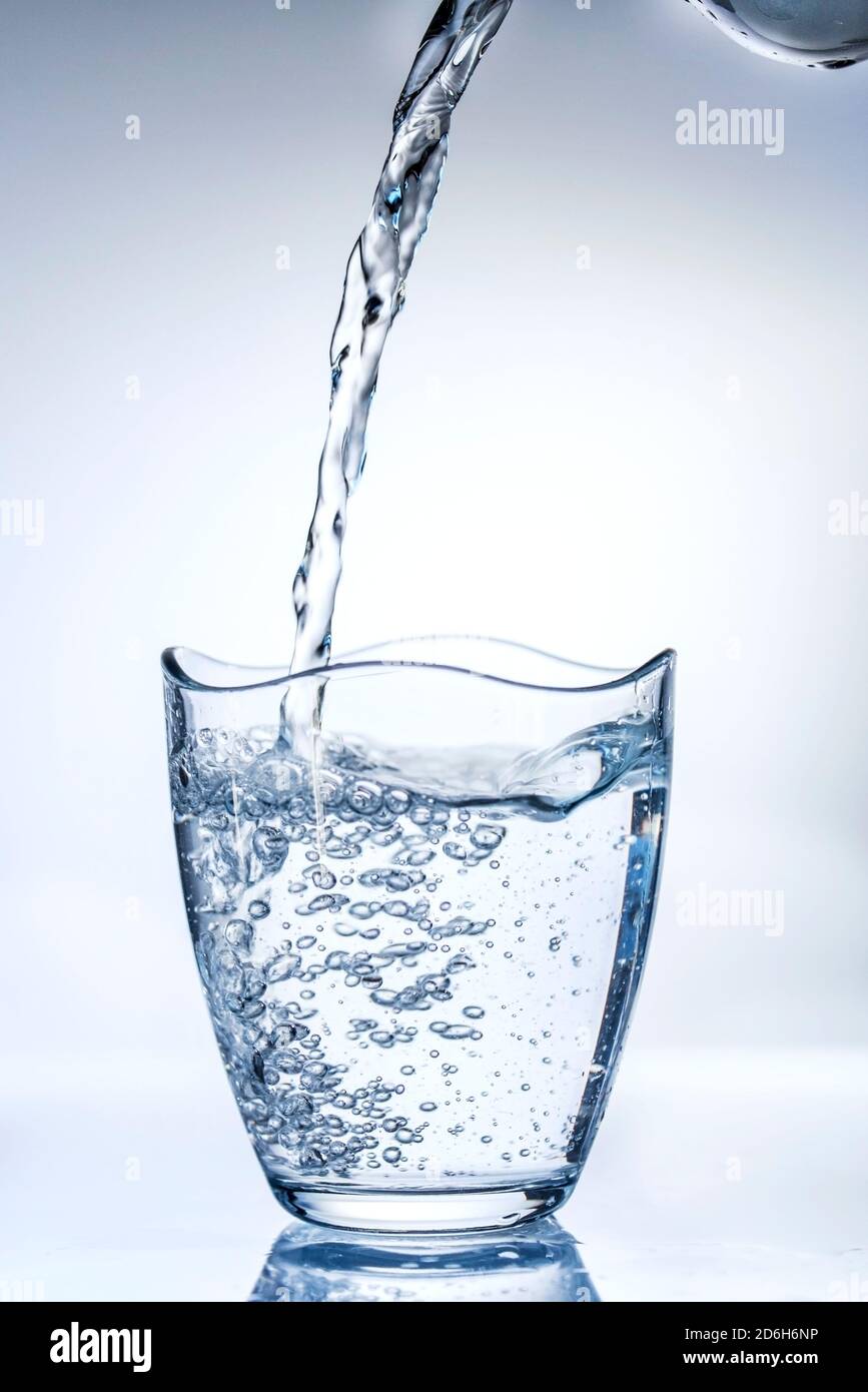 Wasser in ein Glas aus einer Flasche auf weißem Hintergrund, Nahaufnahme, isoliert, Innenaufnahmen Stockfoto