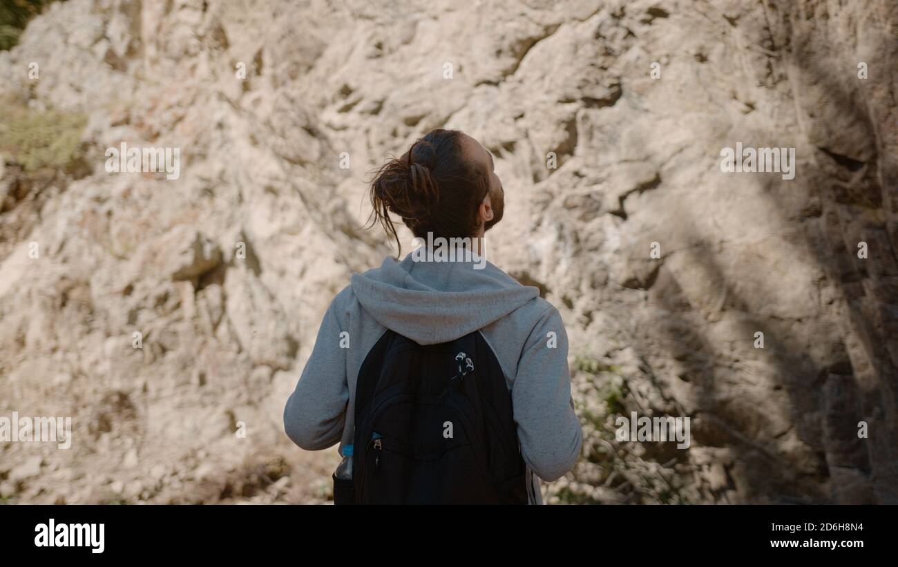 Hippie-Kletterer mit Rucksack hinter sieht einen Felsen im Wald in der Natur und schaut sich es an, Natur Lifestyle-Konzept Stockfoto