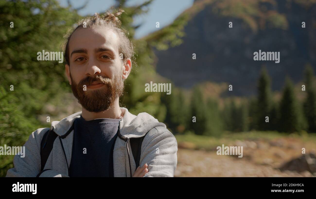 Naturalist lange Haare und bärtige Hipster Mann mit Rucksack Blick auf Kamera und lächelnd, Natur und Lifestyle-Konzept Stockfoto