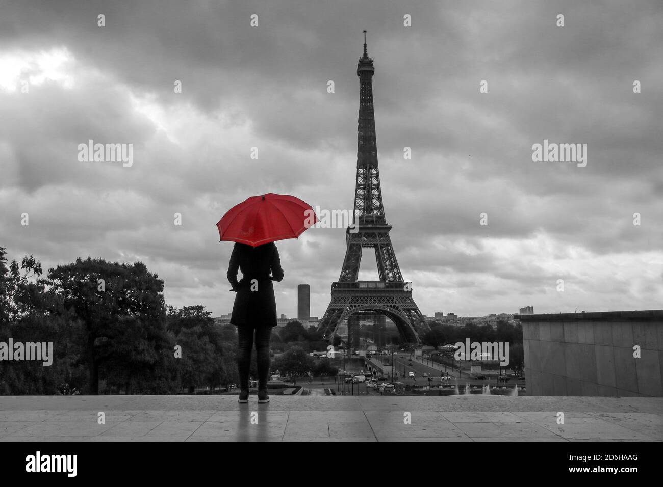 Die Dame mit einem roten Regenschirm steht vor dem Eiffelturm in Paris in Frankreich. Schwarz-Weiß-Bild mit isolierten roten Regenschirm. Stockfoto