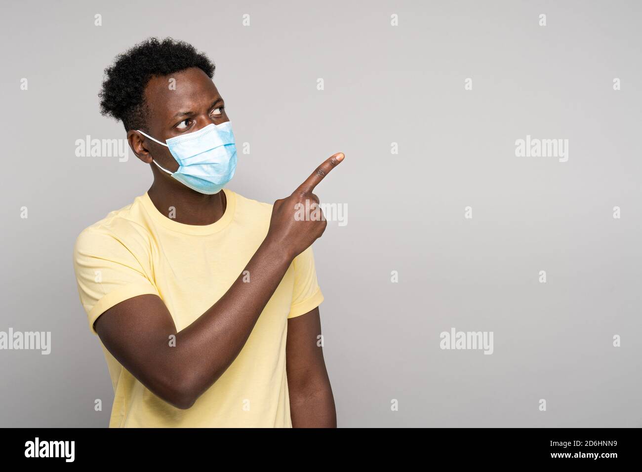 Seriöse Afro-amerikanische Mann tragen Gesichtsmaske zeigt mit beiden Zeigefinger weg, zeigt leere Kopie Platz für Werbung, erinnert an die obligatorische Tragen Stockfoto