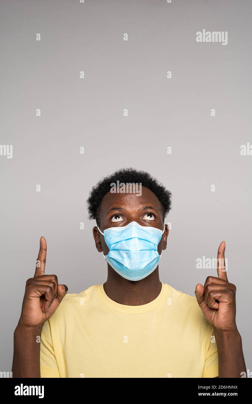 Serious Afro-amerikanischen Mann tragen Gesichtsmaske Punkte mit beiden Zeigefinger, zeigt leere Kopie Platz für Werbung, Angebot, Produkt, Promotion Text, Stockfoto
