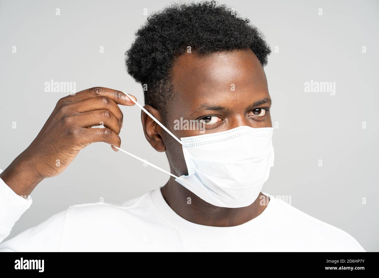 Studio Portrait von afroamerikanischen jungen Mann trägt Gesicht medizinische Maske, Blick auf Kamera, isoliert auf grauem Hintergrund. Schutz vor Grippe, Virus Stockfoto
