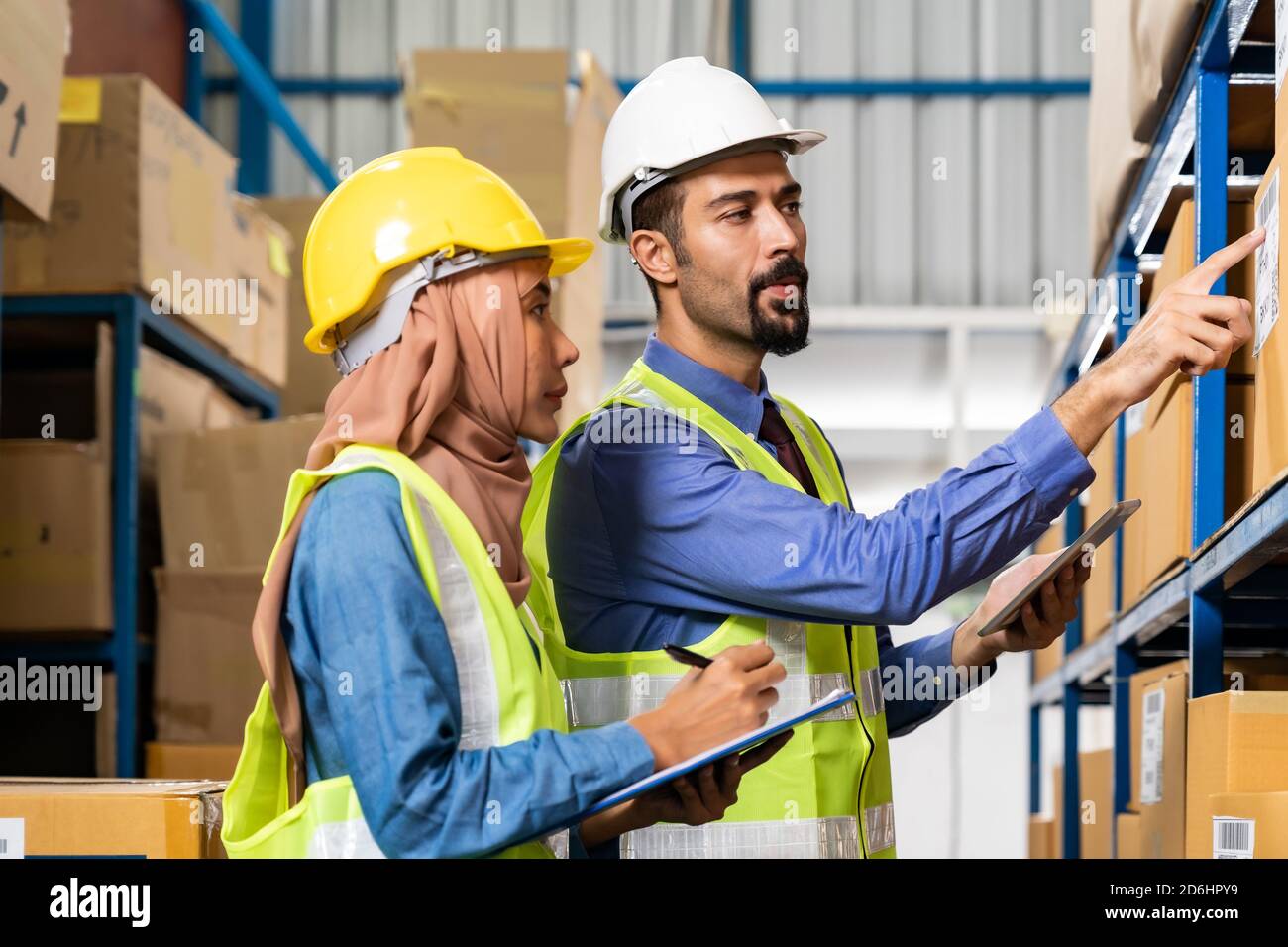 Naher Osten türkischer weißer Lagerleiter Gespräch mit Islam asiatischer Lagerarbeiter über Warenlogistikweg im Verteilzentrum. Für Unternehmen mit Stockfoto