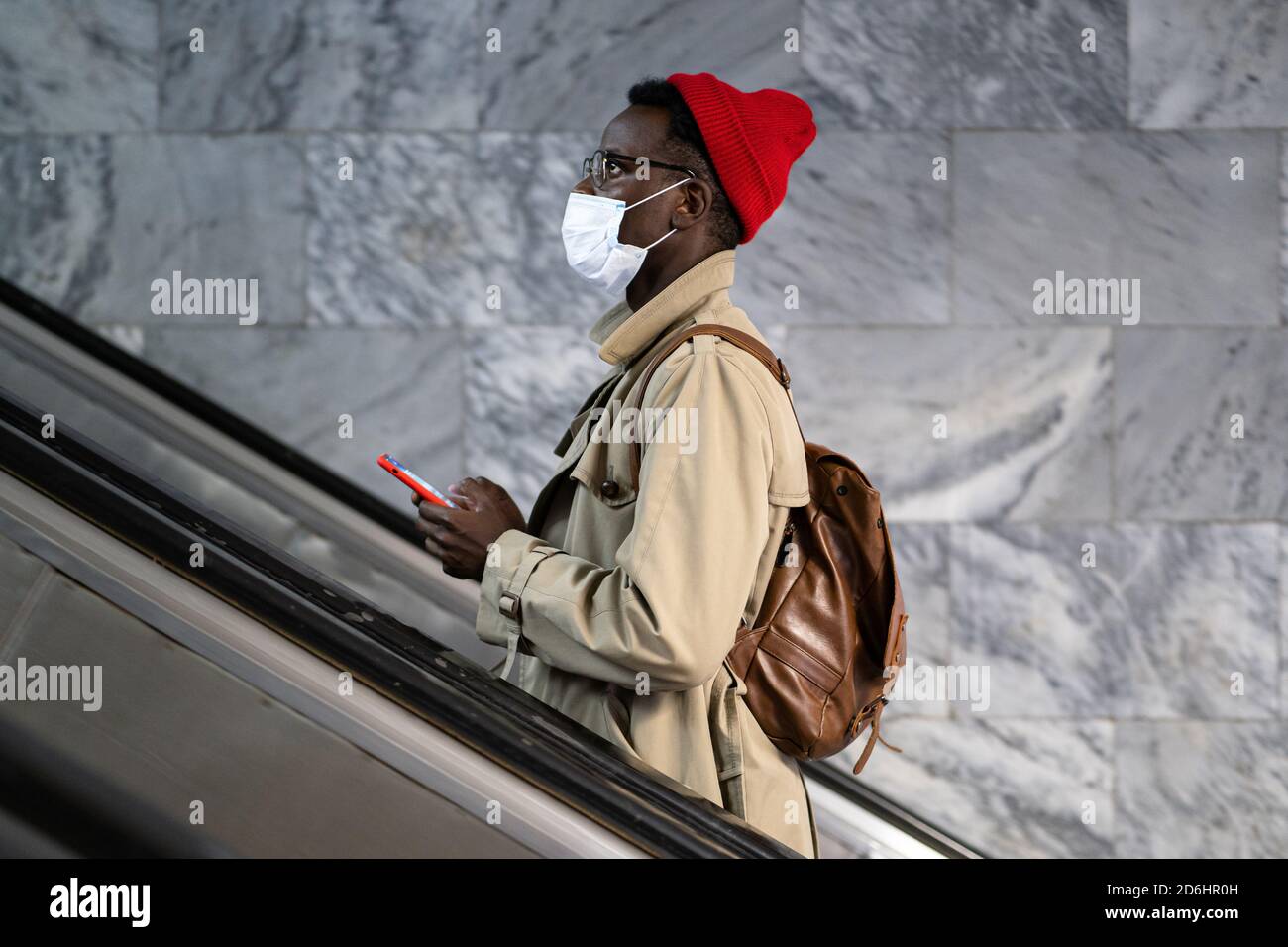 Afro-amerikanischer Reisender Mann steht auf Rolltreppe in U-Bahn oder Bahnhof, tragen Gesicht medizinische Maske, um sich vor Kontakt mit Grippe-Virus zu schützen, p Stockfoto