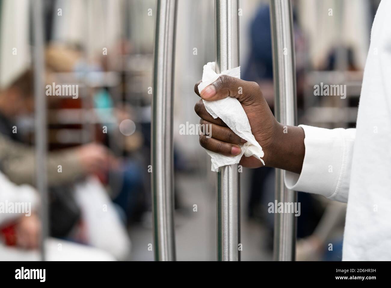 Nahaufnahme von Black man Hand hält einen Handlauf in öffentlichen Verkehrsmitteln oder U-Bahn durch eine Serviette, um sich vor Kontakt mit Viren zu schützen, Keime durin Stockfoto