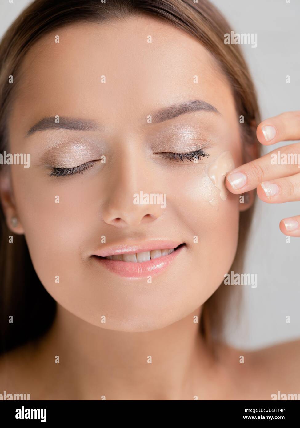 Tragen Sie die Stiftung durch Ihre Hände. Junge schöne Frau macht ihr eigenes Make-up, glatte Haut Ton, Kosmetik und Pflege. Stockfoto
