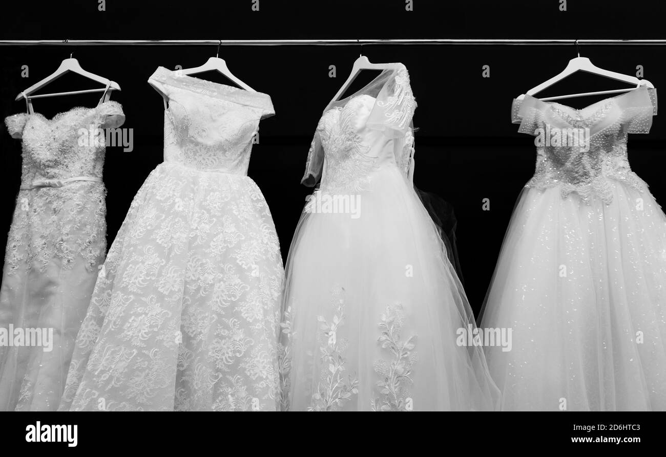 Vier weiße Brautkleider auf schwarzem Hintergrund. Schöne Hochzeitskleider hängen im Laden Stockfoto