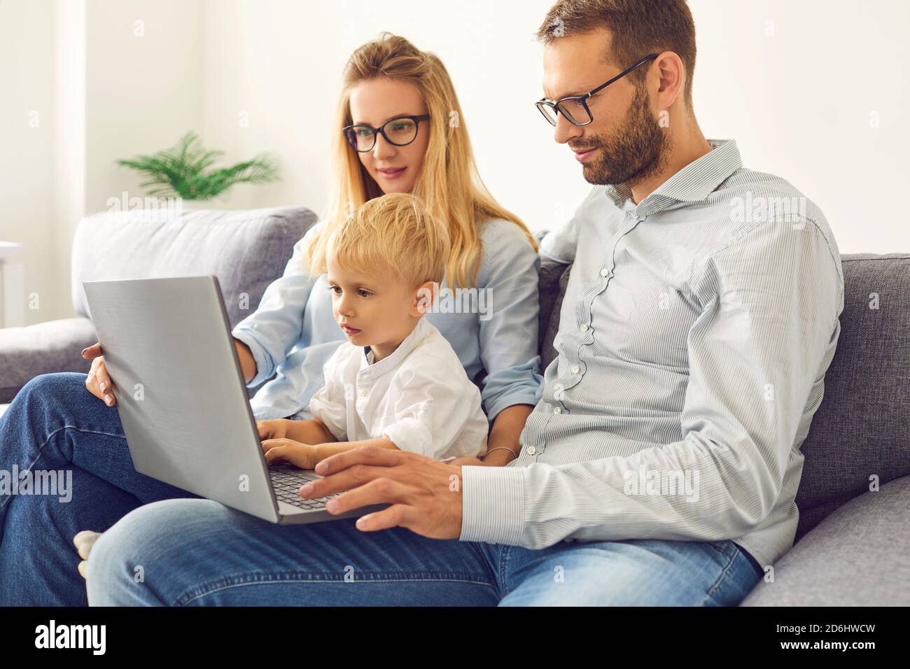 Junge Familie, die zu Hause bleiben und mit einem Laptop Videoanrufe tätigen, Filme ansehen oder online einkaufen Stockfoto
