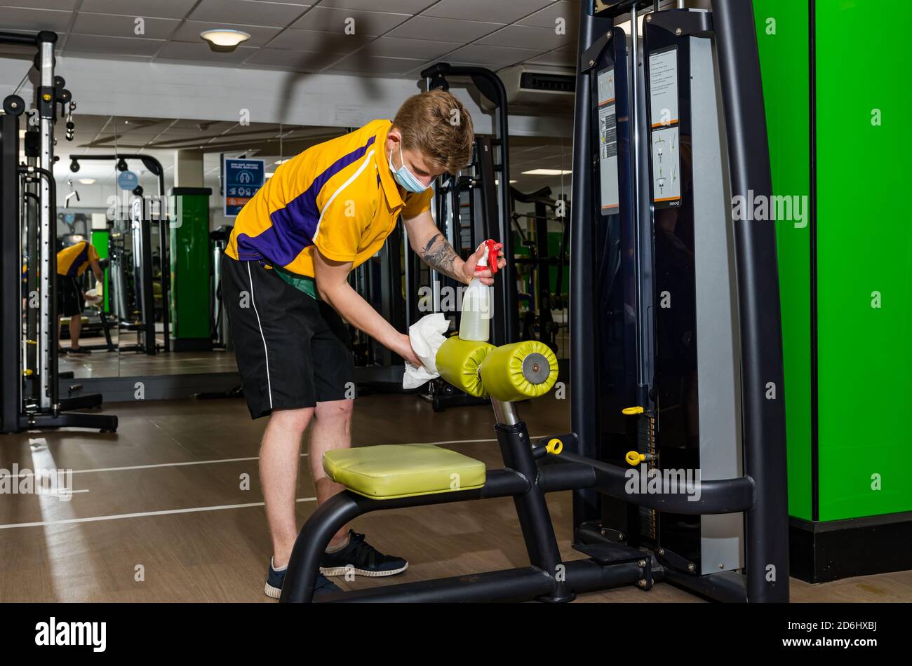 Männlicher Mitarbeiter, der Gesichtsmaske trägt und während der Covid-19 Pandemie im North Berwick Sportzentrum, East Lothian, Schottland, Großbritannien, Fitnessgeräte reinigt Stockfoto