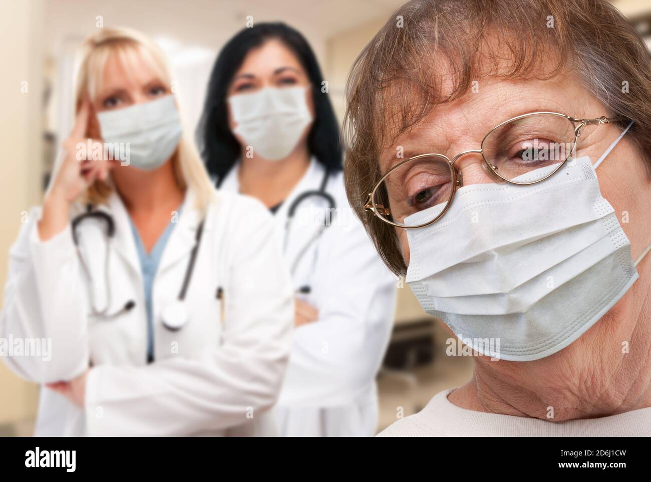 Ältere Erwachsene Frau schaut nach unten, wie Ärzte hinter allen tragen medizinische Gesichtsmasken stehen. Stockfoto