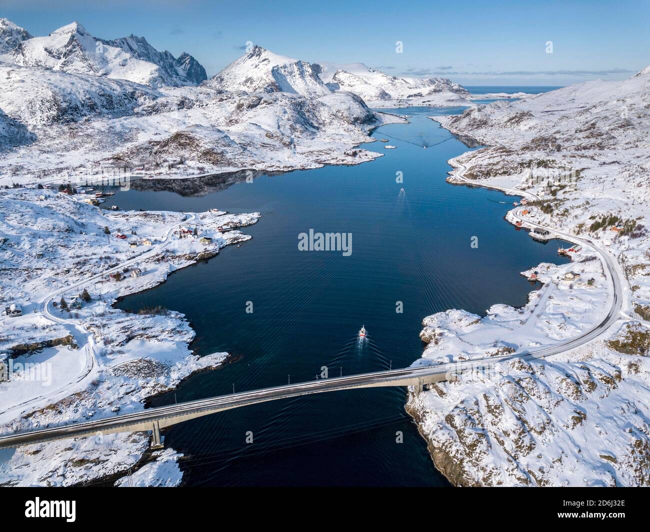 Luftaufnahme, Fjordseeweg mit verschneiten Bergen, Brücke mit Straße und kleinen Fischerbooten, Nordland, Lofoten, Norwegen Stockfoto