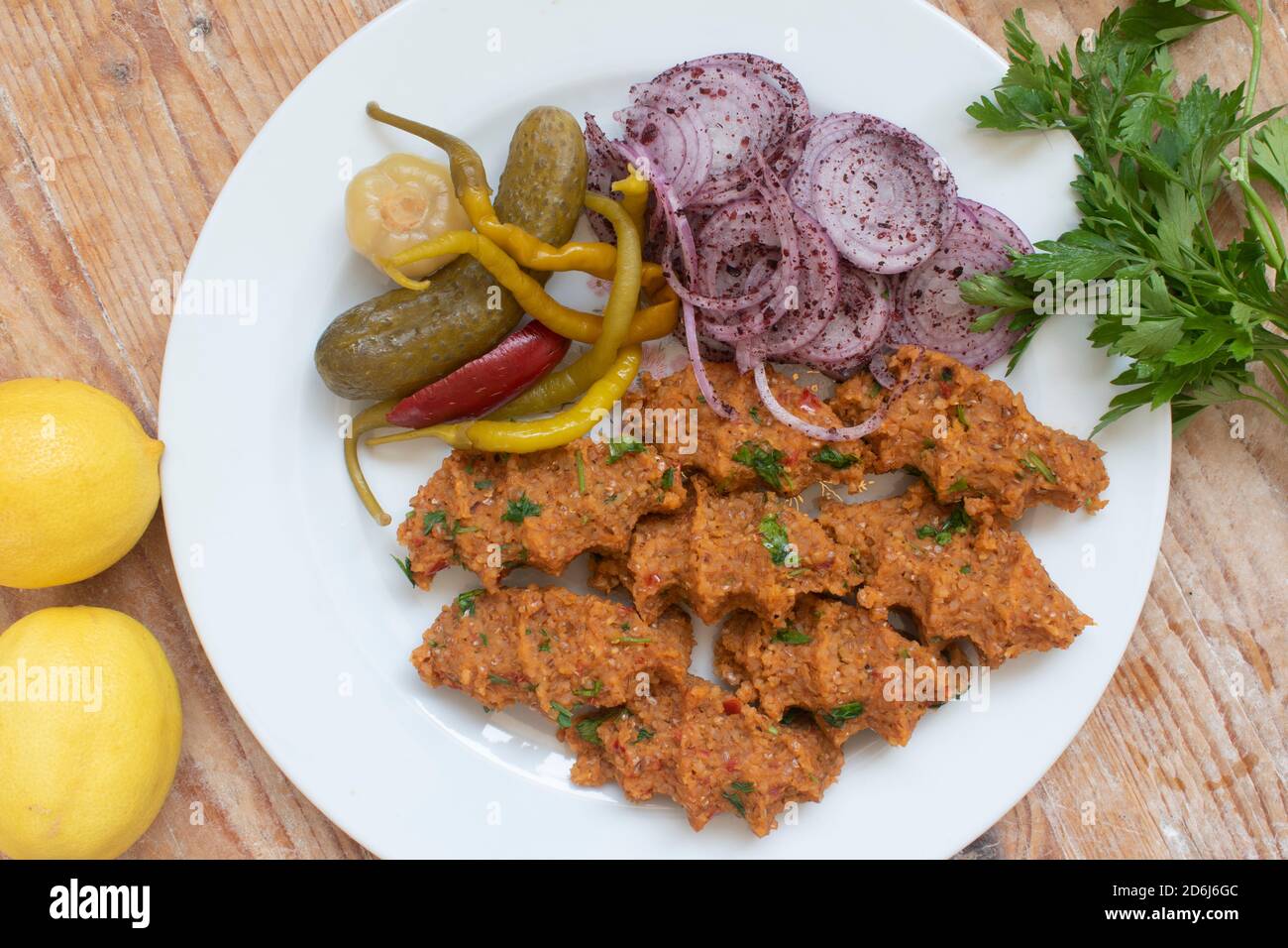 Türkische Küche wird mit Bulgur und Linsen auf einem Teller auf einem Holzboden serviert. Mit Zwiebelsalat, Gurken, Petersilie und Zitrone. Stockfoto