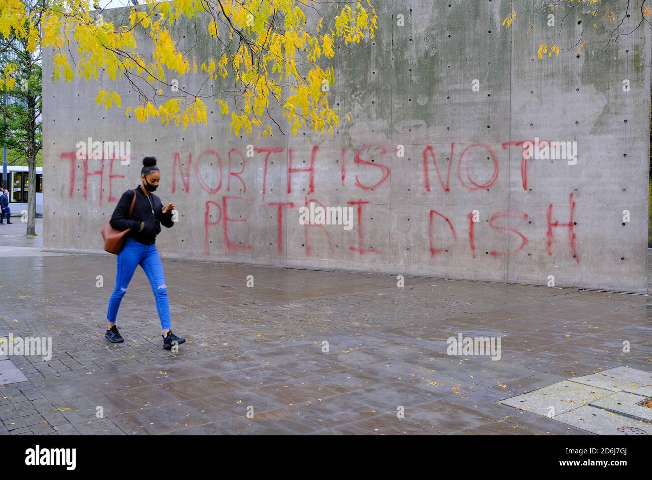 Manchester Piccadilly Gardens Wand mit Lockdown Protest Graffiti BEMALT DER NORDEN IST KEINE PETRISCHALE. Frau in Maske gehen daran vorbei. Stockfoto