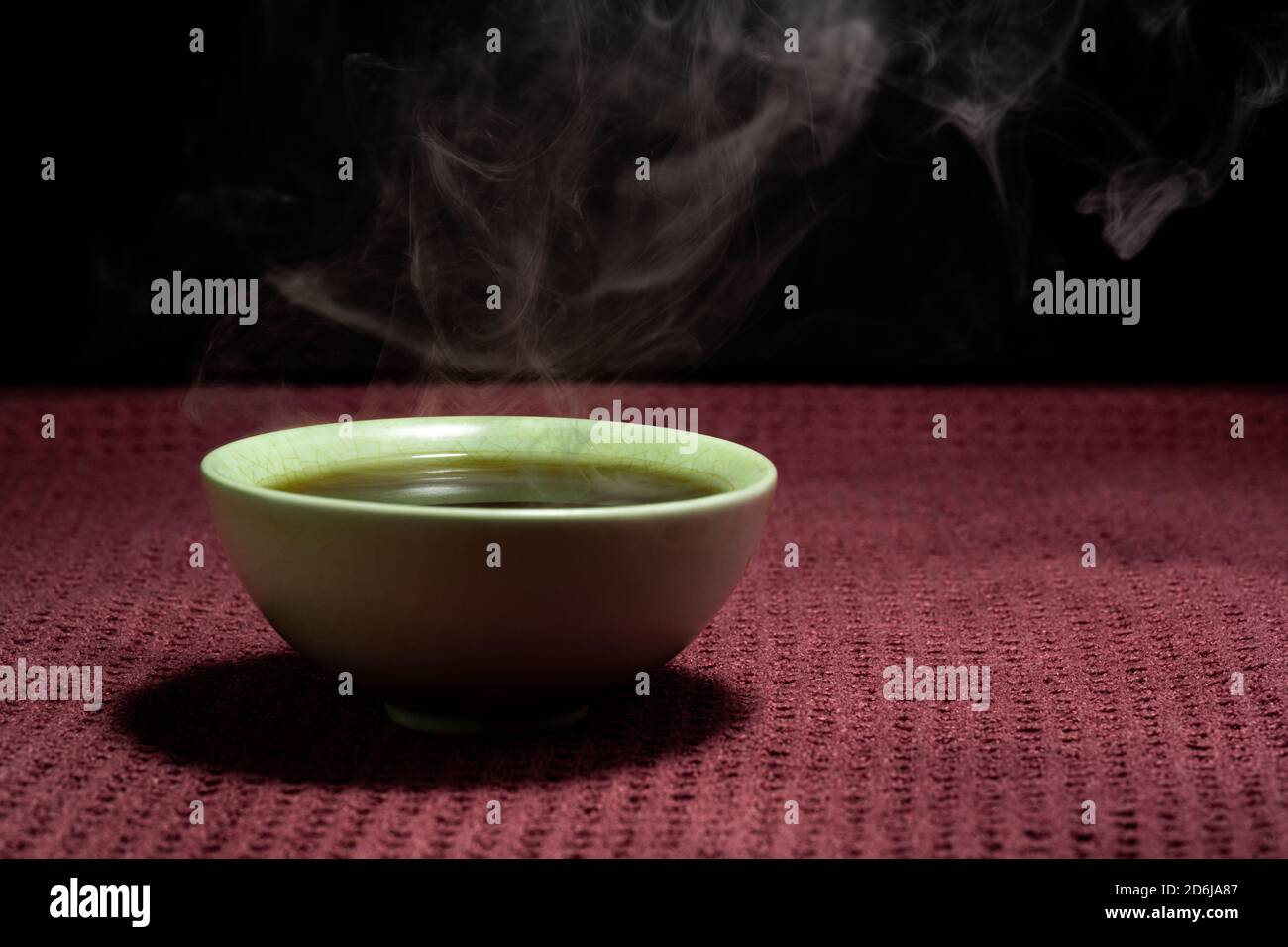 Chinesischer Tee dampfend in einer kleinen grünen Teetate isoliert mit Ein schwarzer Hintergrund und eine rote Oberfläche Stockfoto