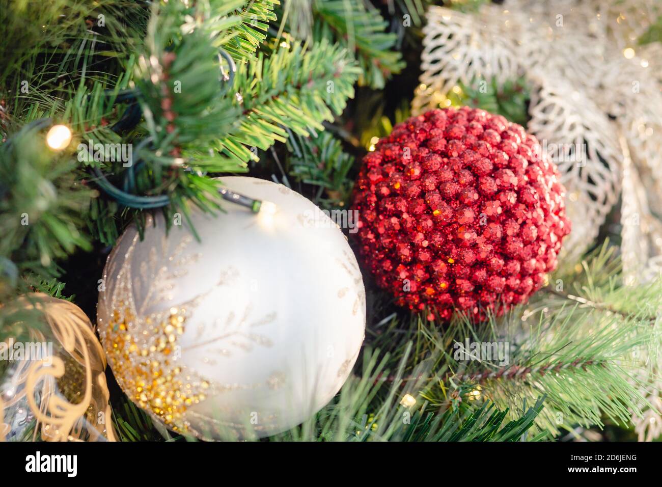 Weiße und rote weihnachtsbaumkugeln auf Tannenzweig mit Lichtern. Weihnachtsschmuck auf den Weihnachtsbaumkugeln Girlanden. Stockfoto